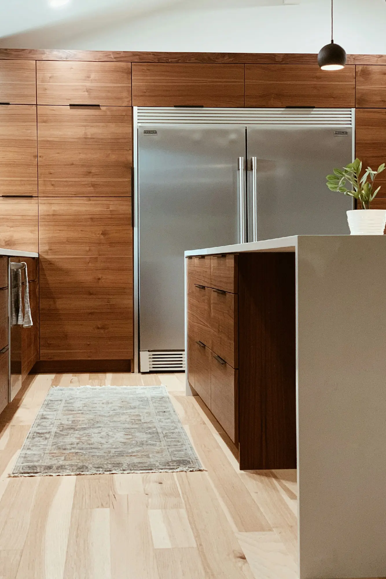 A modern kitchen interior featuring warm wood cabinetry and a large stainless steel refrigerator, showcasing the high-quality cabinet staining and finishing services provided by Grayton Painting..